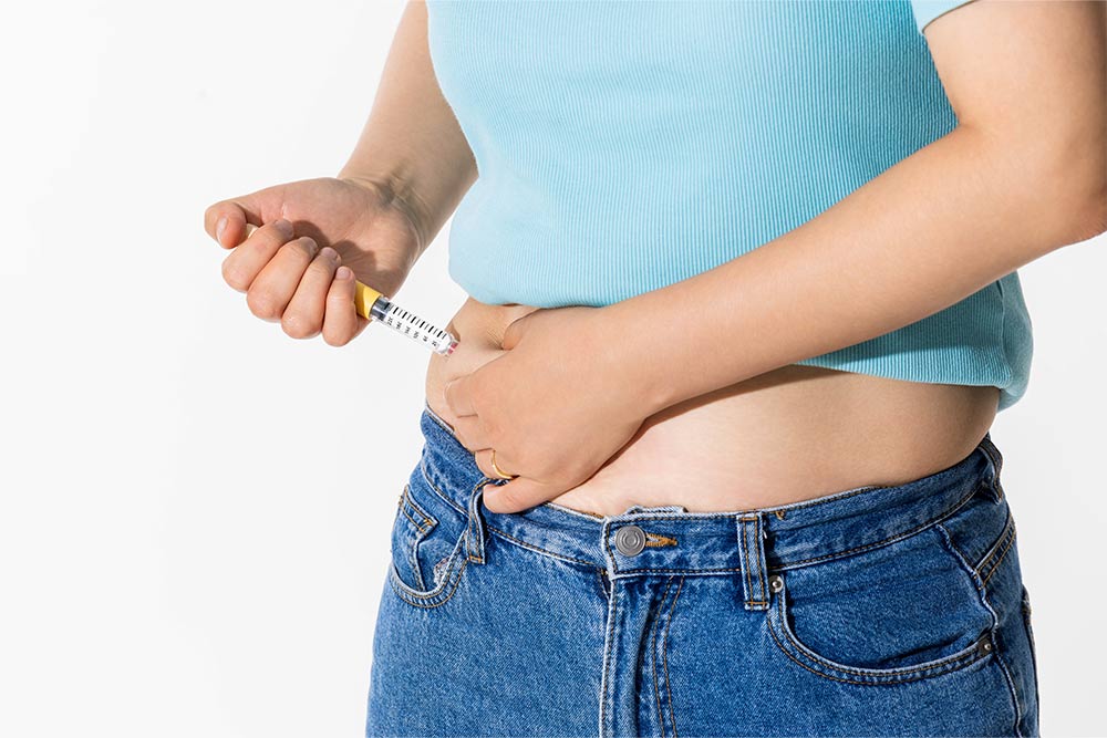 A person wearing a blue shirt holds a weight loss injection and sticks it in their stomach.